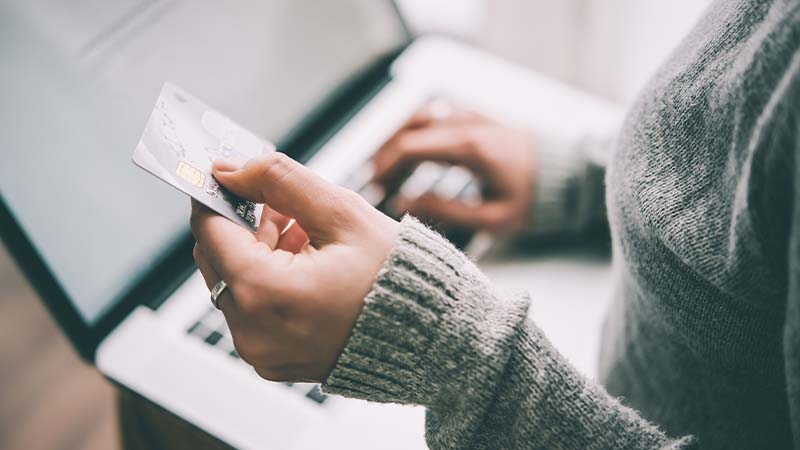 Eine Person bedient mit ihrer rechten Hand einen Laptop, während ihre linke eine Bankkarte hält