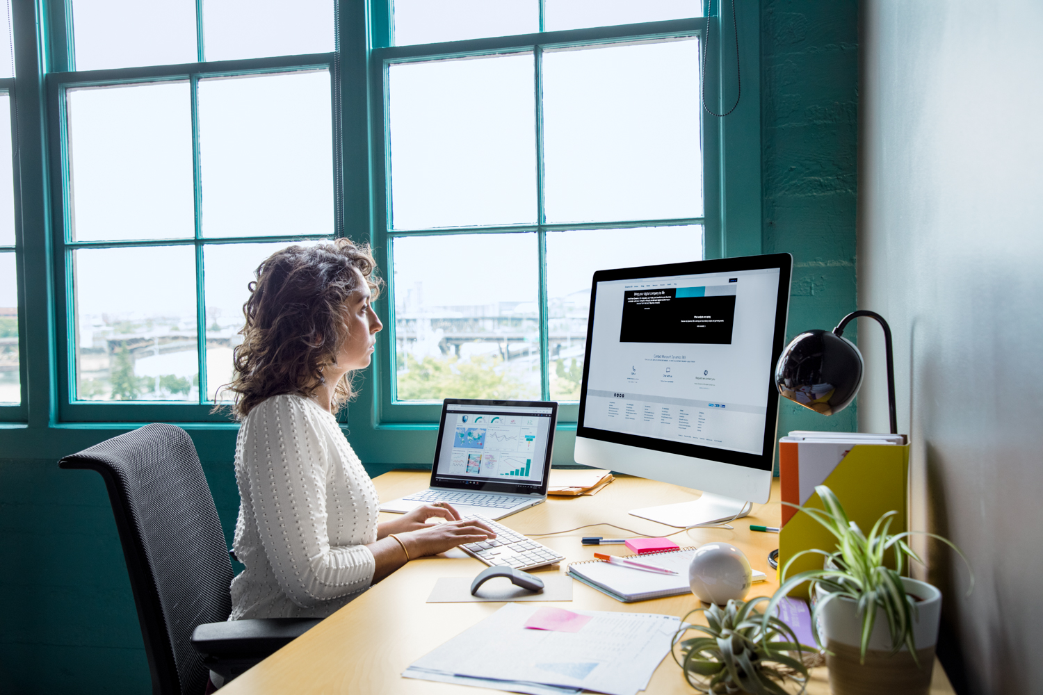 Office worker sitting at desk using an all-in-one computer in casual office with a laptop also on desk