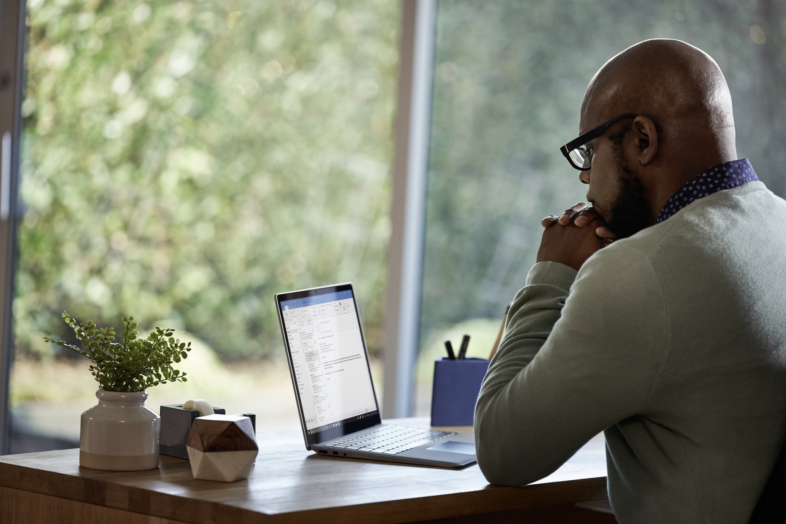 Male working remotely from his home office on a Dell Latitude 13 device. This image is available with two different screen options: one showing the device running Microsoft Outlook, and another showing a Microsoft Teams conference call with 9 people on the screen