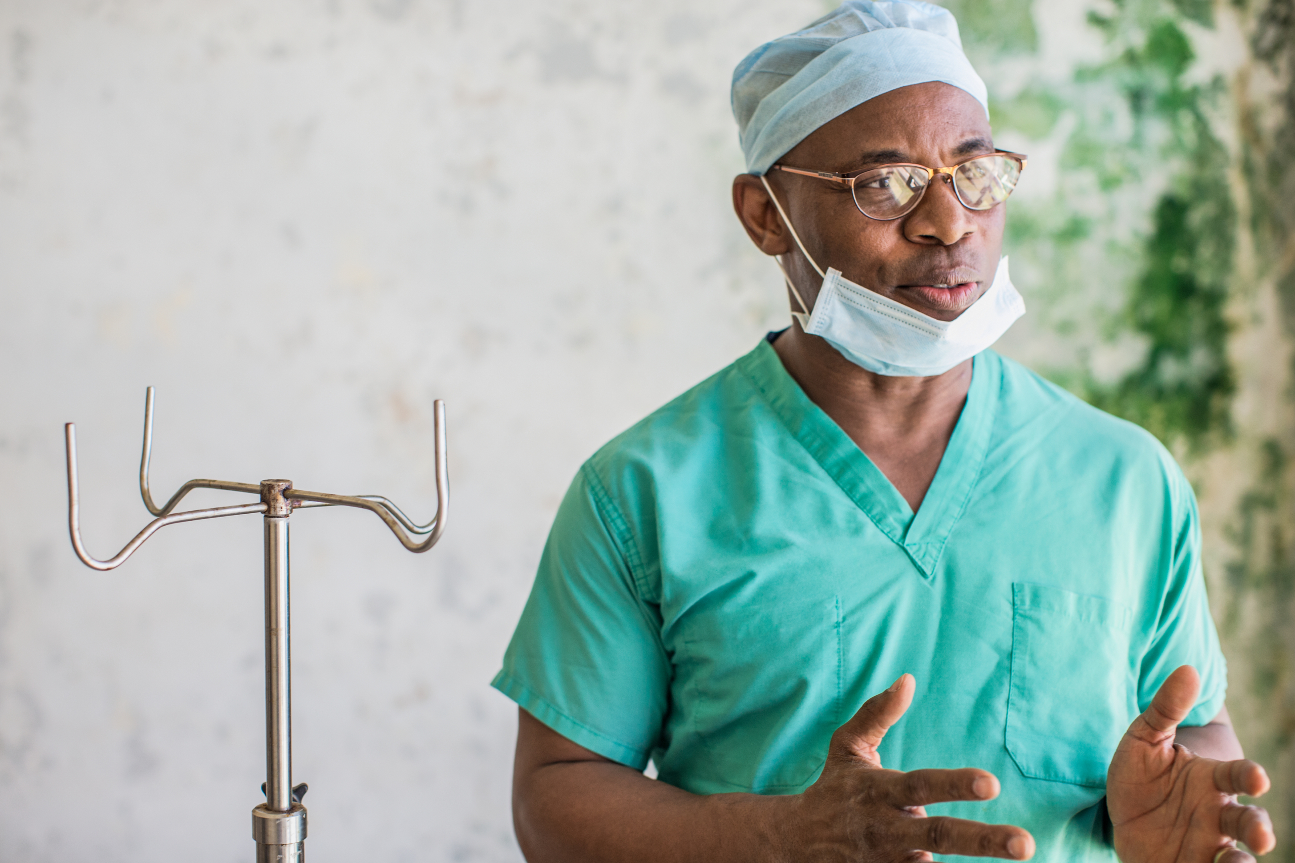 Real people. Male doctor wearing scrubs, glasses, and face mask standing and speaking in medical facility in Liberia