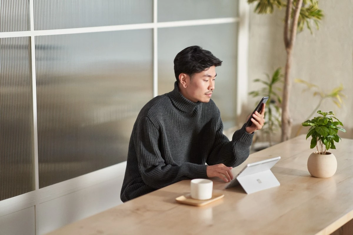 Customer using secure multi-factor authentication on a mobile phone and a tablet while working remote from a caf&eacute;. Keywords: One person; mobile device; WFH; security; on the go; man; male; authentication; MFA; identity access and management; secure access; hybrid work; end user; security