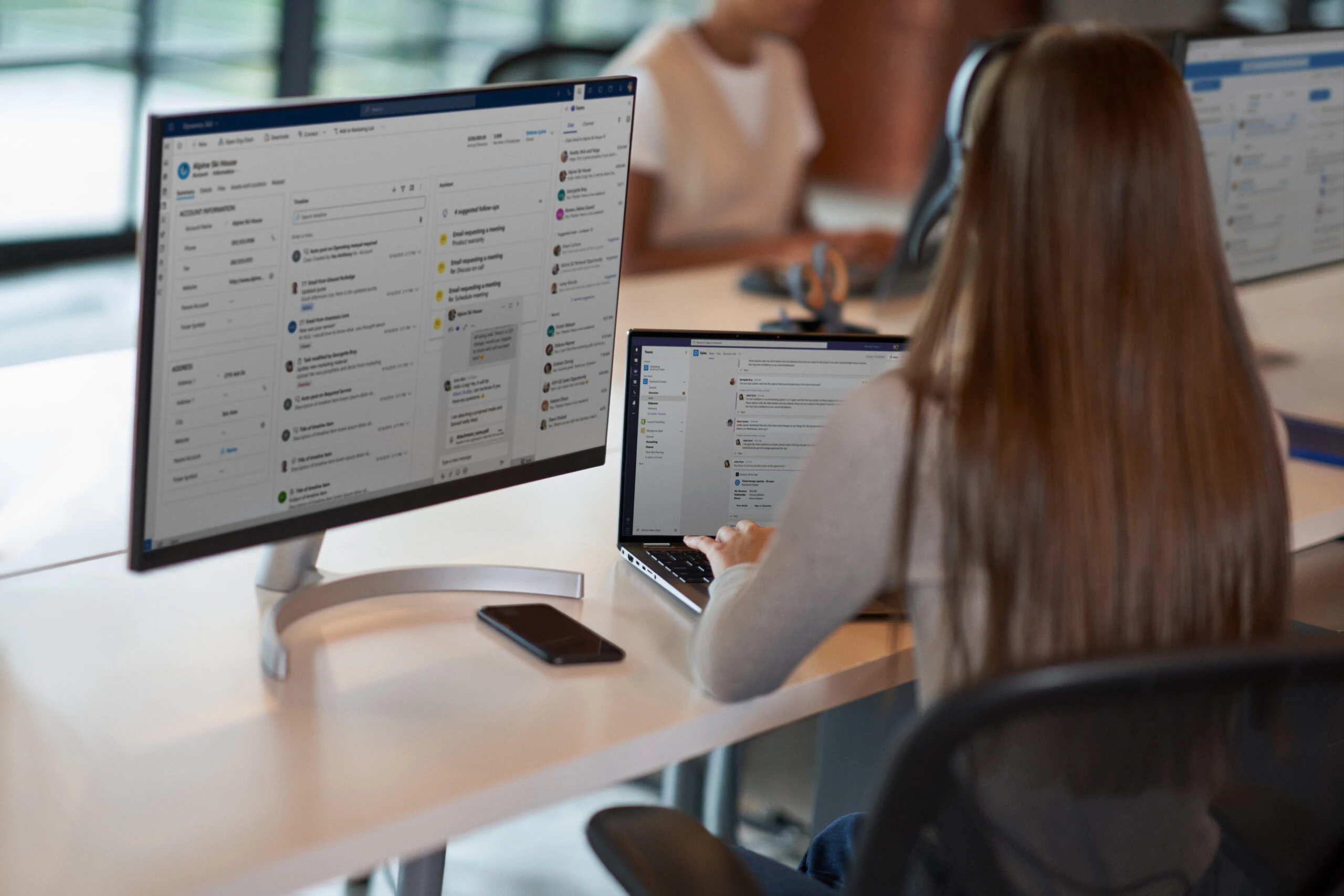 A woman sitting at a desk with two monitors, working on a customer service call