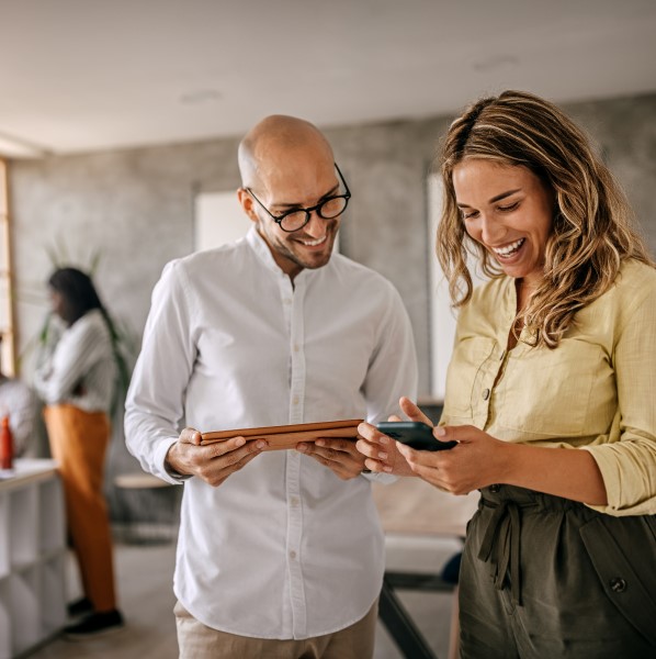 Two employees standing together, one holding a tablet and the other holding a phone that theyre both looking at