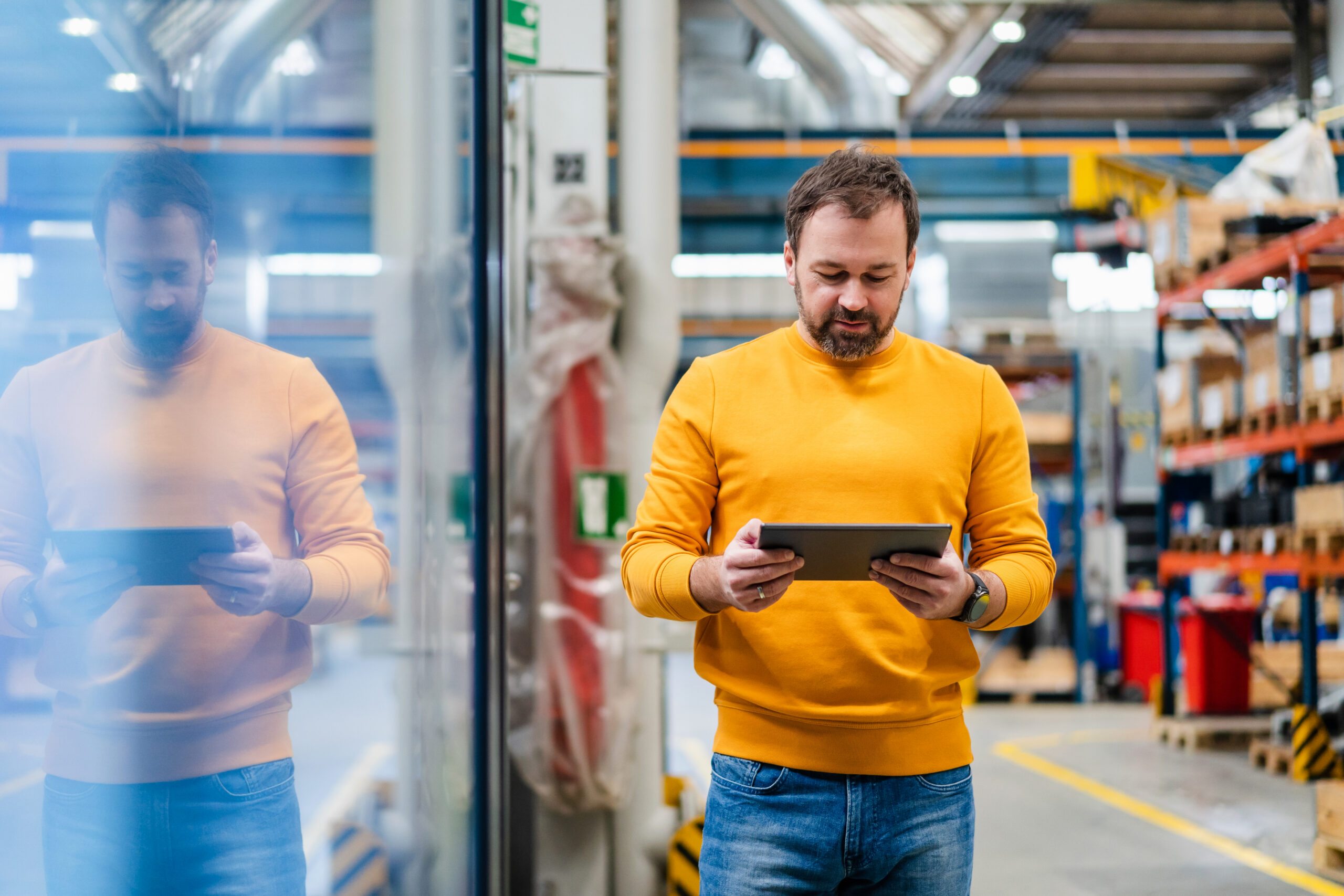 Person reviewing information on a tablet while standing on a warehouse floor with storage shelves in the background