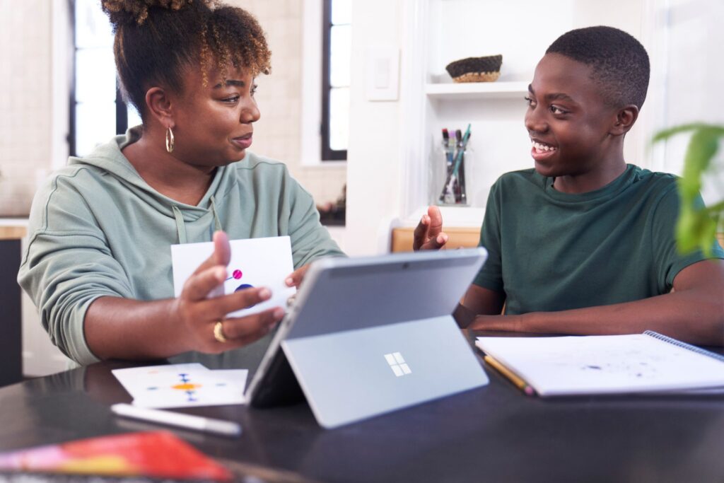 A teacher engages with a student at a desk.