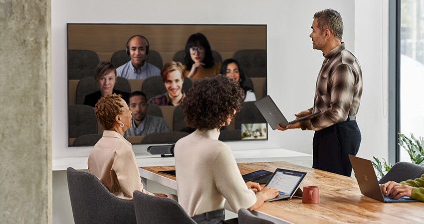 Four Coworkers in a meeting room, while having people on a video call through a big screen