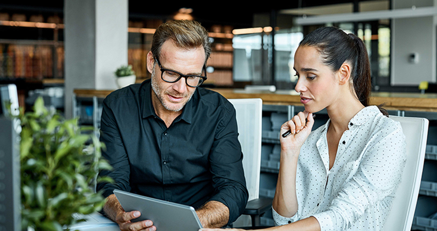 A man and woman are engaged in conversation while examining a tablet together