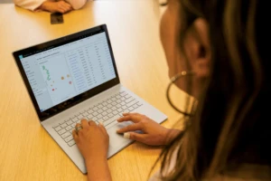A woman using a computer. She has a data dashboard on the screen.