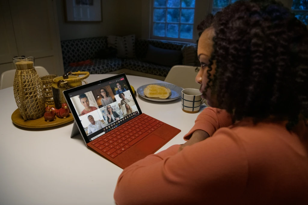 A woman using a laptop computer sitting on top of a table. She is in a Teams meeting.