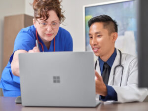 Two medical professionals talking about something on a laptop screen in front of them.