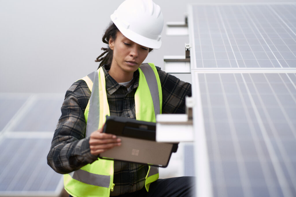Field engineer inspects solar panels on a wind farm using remote assist on a Surface tablet.