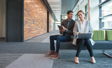 Image of two co-workers consulting one another on a bench outside a meeting room