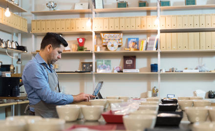 Image of a bakery owner and operator working on his laptop amid bowls and coffee cups