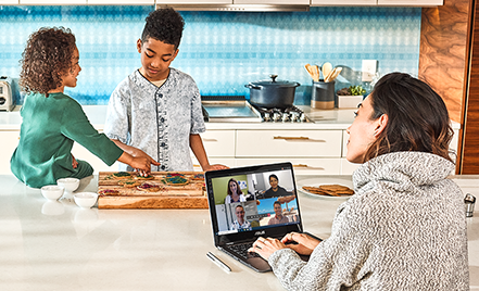 Image of a remote worker in a Microsoft Teams meeting while her children eat across from her on the kitchen countertop