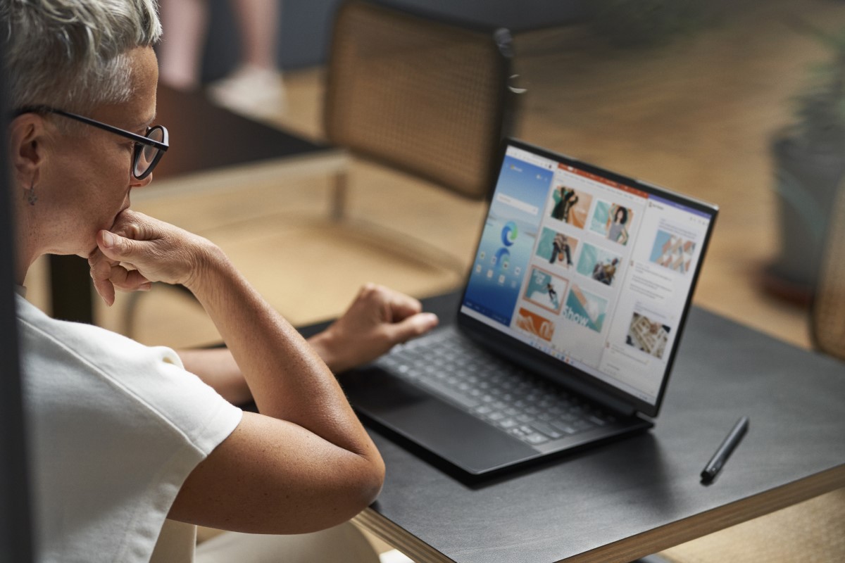 Adult sitting at table, looking at laptop with Edge, PowerPoint, and Word on screen via Snap feature. Keywords: table; over the shoulder; remote workplace; meeting; caf&eacute;; New York City