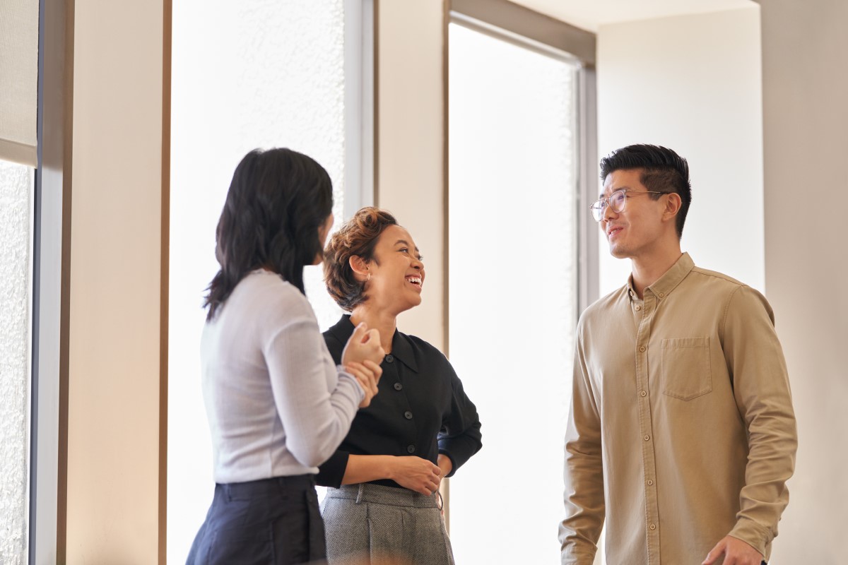 Two women and a man having a conversation standing in an office hallway