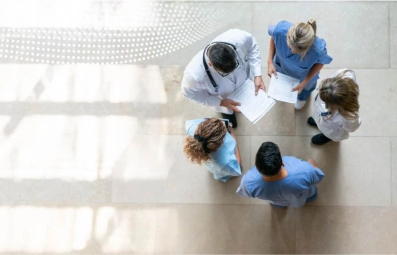 An overhead shot of a group of medical professionals standing in a circle in conversation on a beige tiled floor