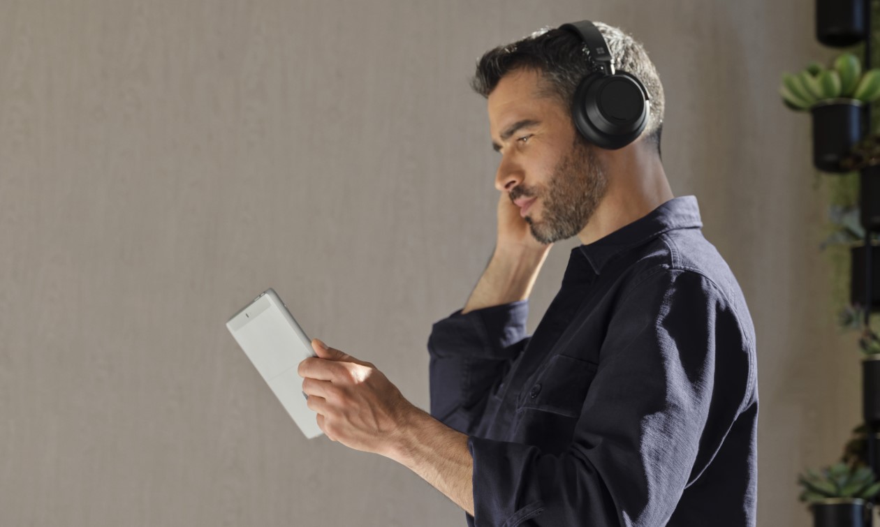 Adult male holding a platinum Surface Go 4 (Go 3) in tablet mode while wearing Surface Headphones 2+