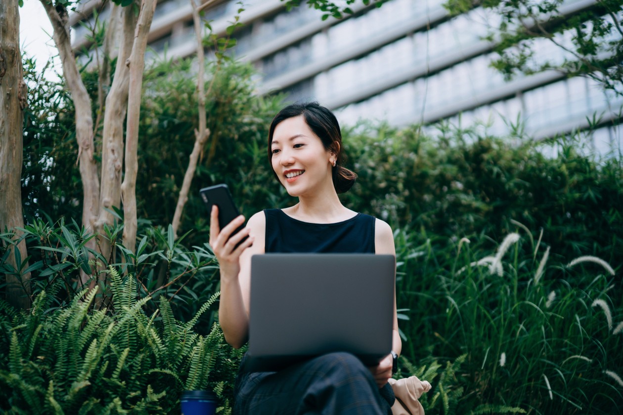 Woman working with laptop outdoors in urban office park, surrounded by green plants