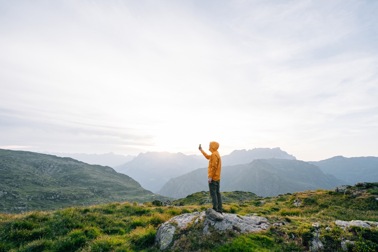 Young man takes photo with cell phone at sunrise on an alpine meadow