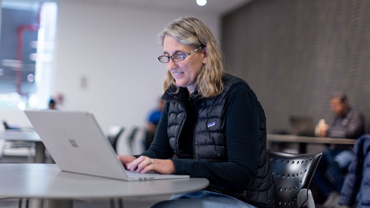 Woman in black vest and shirt typing on a laptop in a cafe