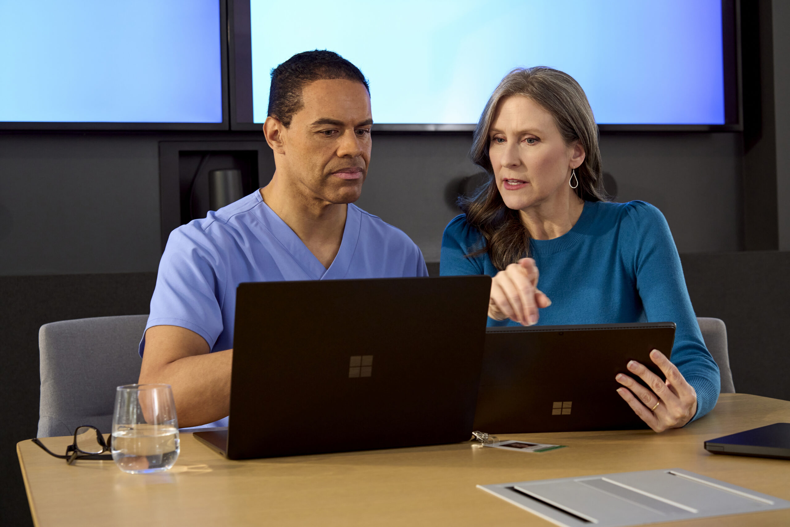 Male clinician and female hospital administrator looking at a computer and tablet in a conference room