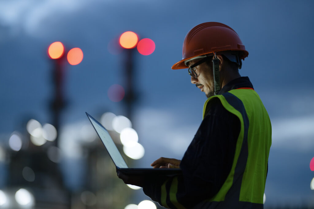 Boosting Key Front-line Operations Through Digitization to Driving Sustainability in Oil and Gas Industry. Side view of Engineer working over a laptop computer to analyze insights related to the production of energy in field operation