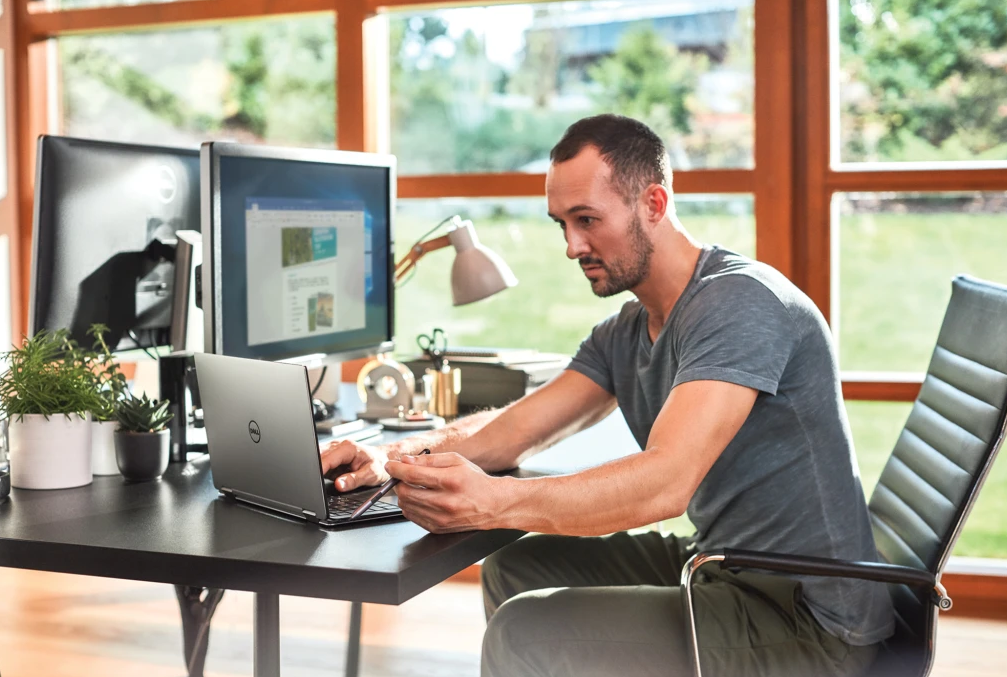 A man sitting at a laptop working by an open window