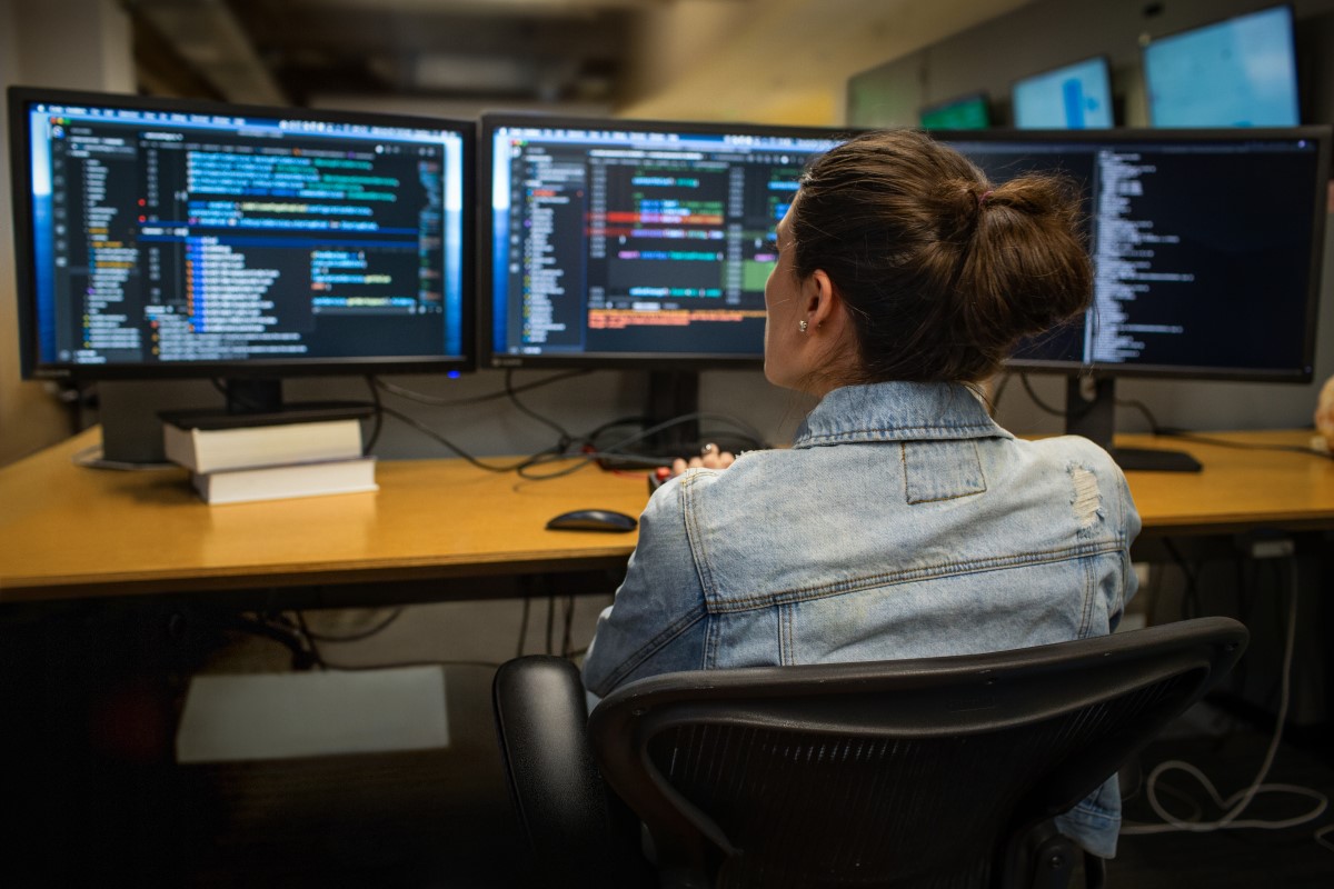 Real people, real offices. Female developer coding her workspace in an enterprise office, using Visual Studio on a multi-monitor set up. Mechanical keyboard. Women who code, women developers, women engineers, code, develop, Black developer, engineer, Visual Studio, Azure