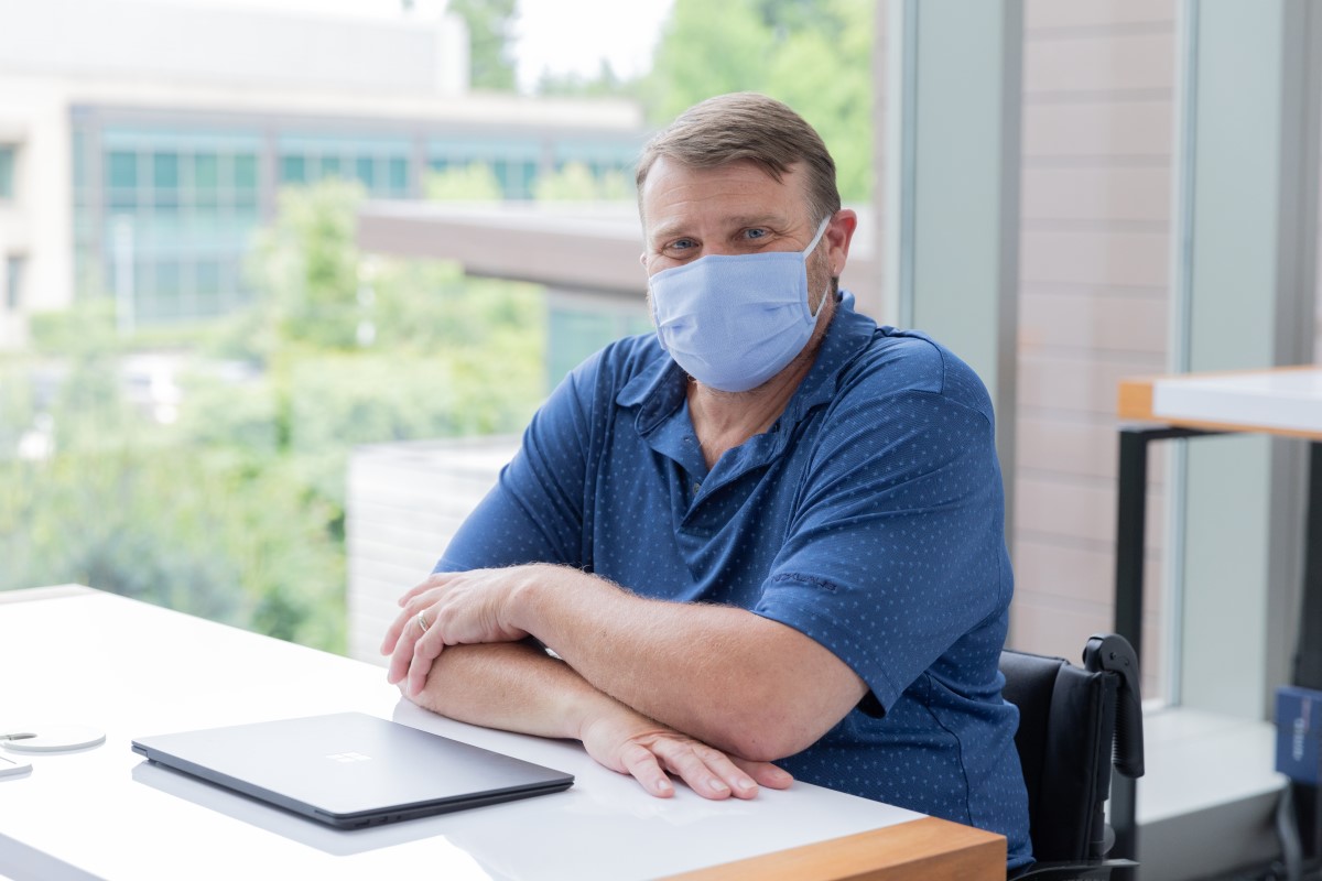 A male employee in a wheelchair wearing a face mask and smiling at his desk. Hybrid Workplace collection