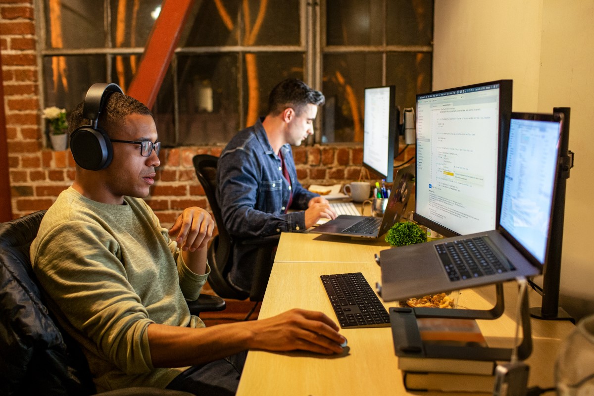 Two male developers in focused work in n casual enterprise office. One is wearing headphones