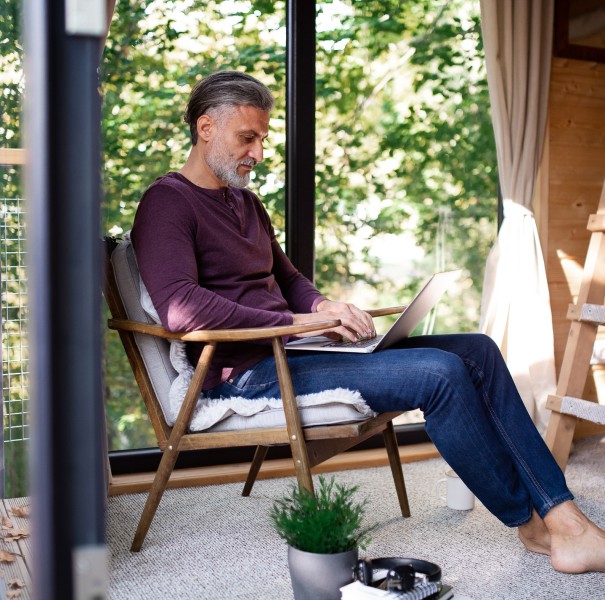 A mature man sits inside a treehouse, using a laptop