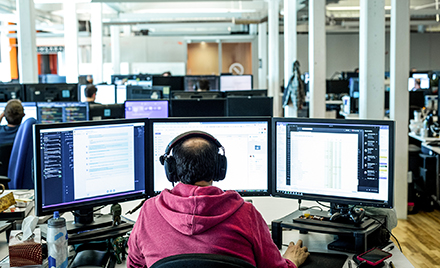 Image of a tech worker working on three monitors