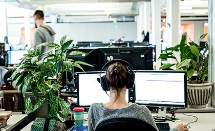 Image of a woman wearing headphones and looking at two computer monitors