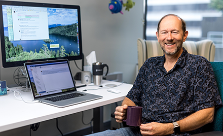 Image of a developer sitting with a cup of coffee at his desk