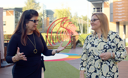 Two women talk outside a corporate office building with art in the background
