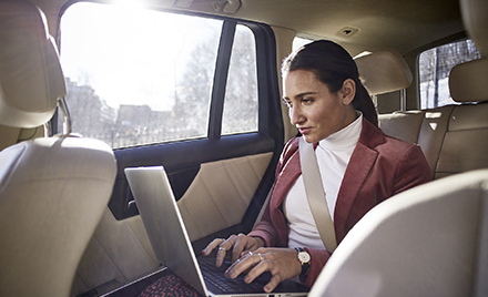 A woman in a car types on her laptop