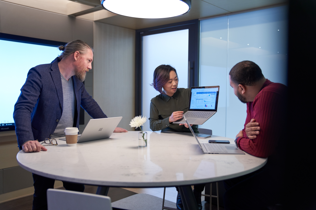 Woman and two men working in a meeting room all with Surface laptops