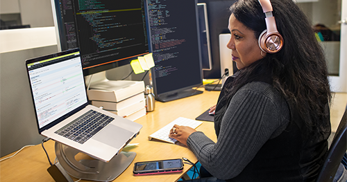 An image of a female developer coding at her desk, wearing headphones
