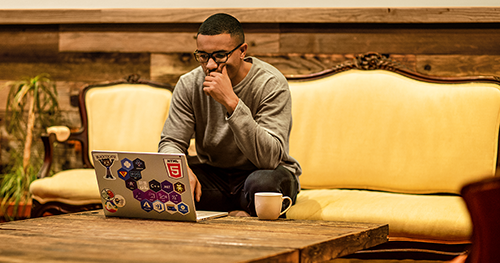 An image of a man sitting on a couch working remotely with his laptop