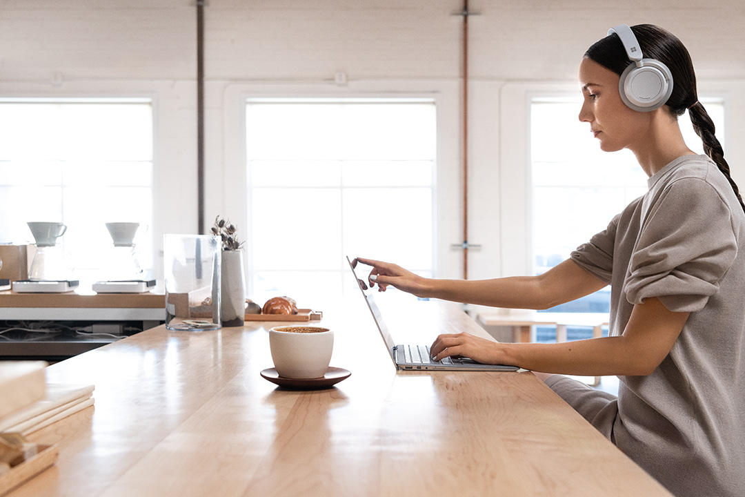 Contextual image of woman wearing Surface headphones working on Surface Laptop2 inside