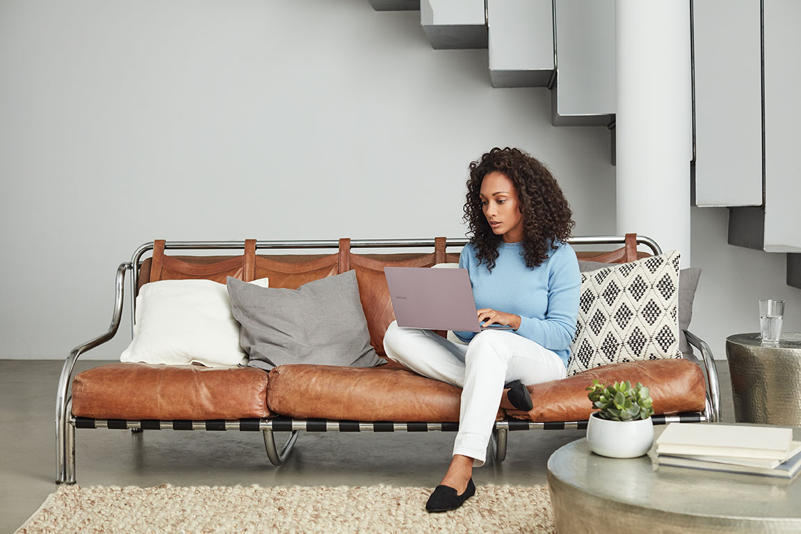 Adult inside home working, sitting on a brown couch, looking at a computer