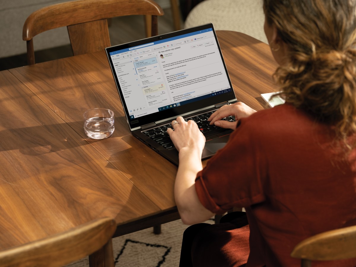 Over the shoulder photo of an adult woman at her dinning table looking at her Microsoft Outlook inbox