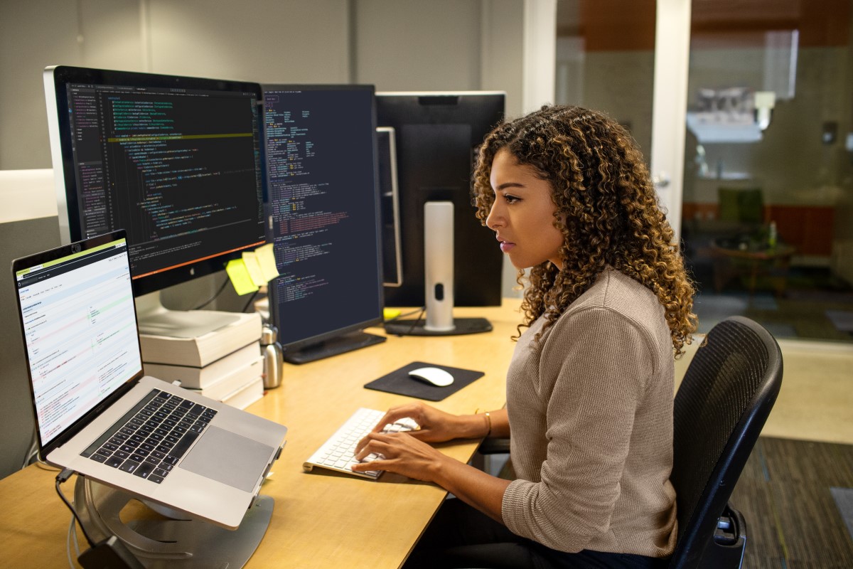 Black female developer working at enterprise office workspace. Focused work. She has customized her workspace with a multi-monitor set up