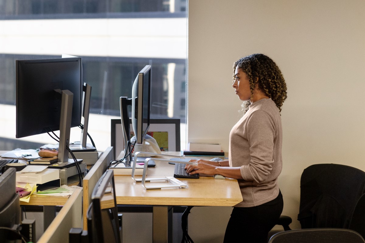 Real people, real offices. Black female developer doing focused work at a standing desk in enterprise workspace