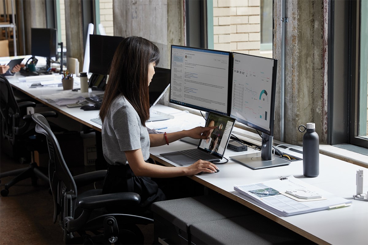 Adult female sitting at a desk in an office environment with a Microsoft Surface Laptop 3 using touchscreen to scroll