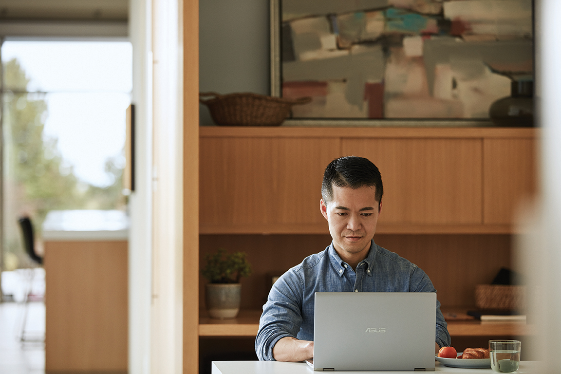 Adult male mobile professional on the go with ASUS ZenBook. Working at kitchen table with glass of water
