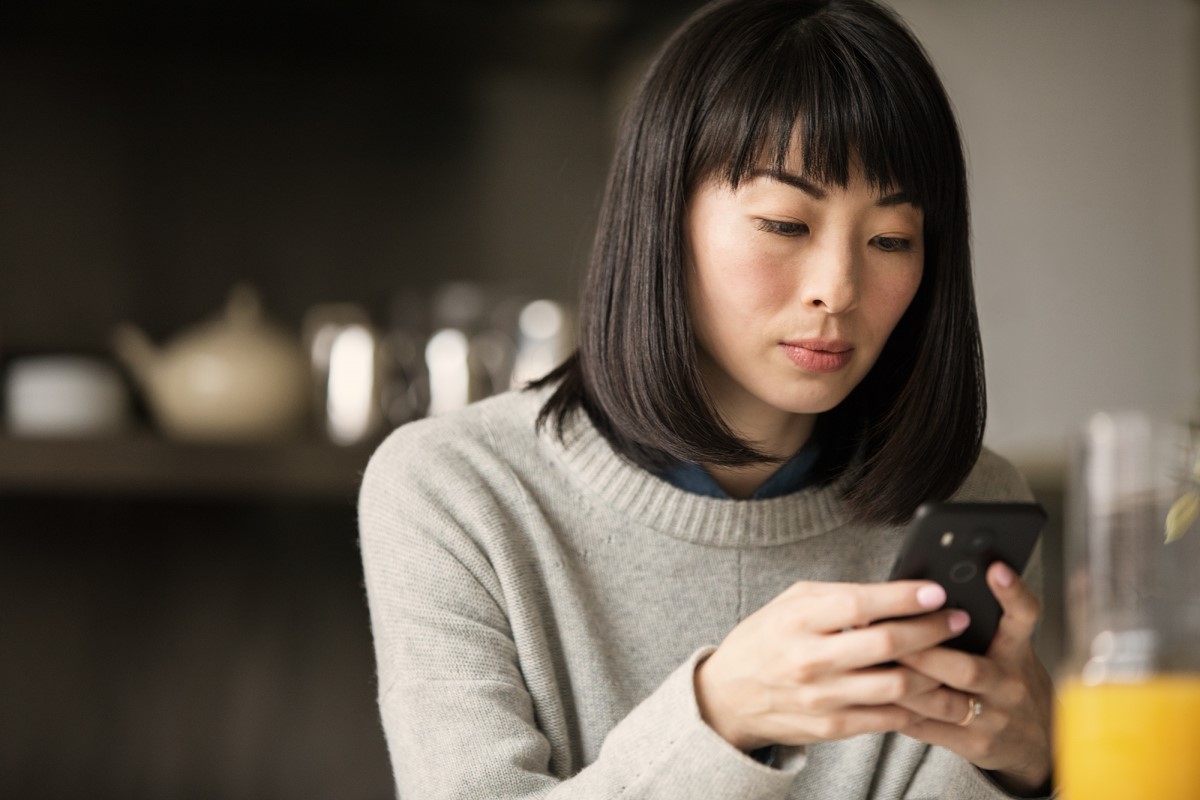 Adult female looking at phone with glass of juice in foreground