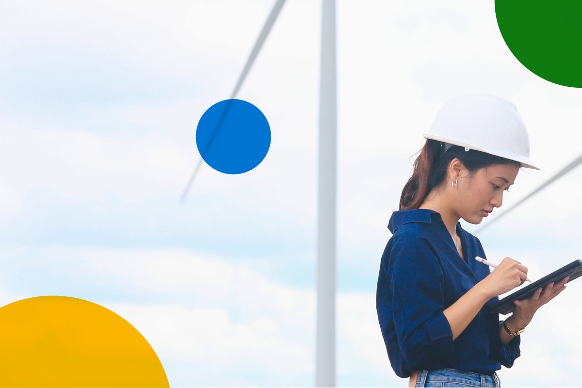Field worker with wind turbines in the background working on hand held device