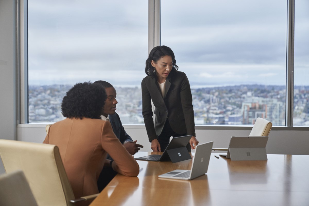 Conference room table with four people in a meeting with Surface Laptop Go 2 and Surface 2-in-1&lsquo;s